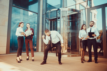 A young male businessman is enjoying a successful deal on the background of office workers. Demonstration of positive emotions and gestures. Career. Success. Shows a thumbs-up.