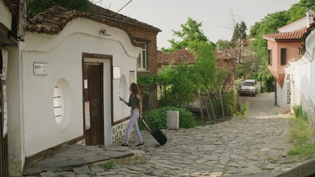 Wide slow motion shot of woman with suitcase knocking on door of house / Plovdiv, Bulgaria