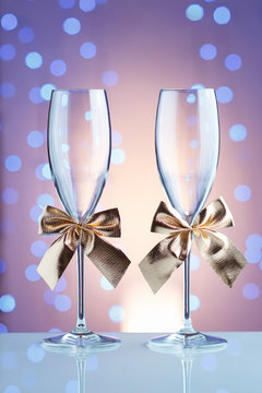 Festive champagne glasses with golden bows on a glass table with a beautiful blue bokeh