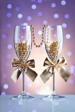 Festive champagne glasses with golden bows and beads on a glass table with a beautiful blue bokeh