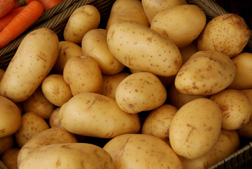 Basket of Fresh Potatoes next to a basket of Fresh Carrots at a Vegetable Market Stall