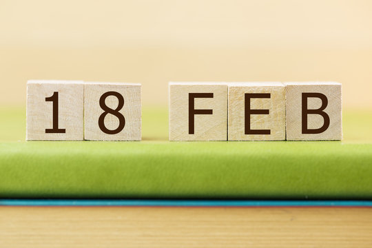 Wooden cube shape calendar for FEB 18 on green book, table. 