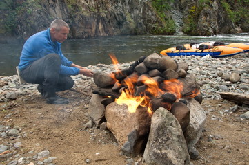 Man heat the hearth for the hiking Russian bath on the bank of the river.