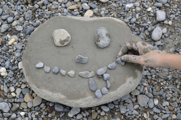Mano de niño construyendo una cara con barro y guijarros sobre una piedra.
