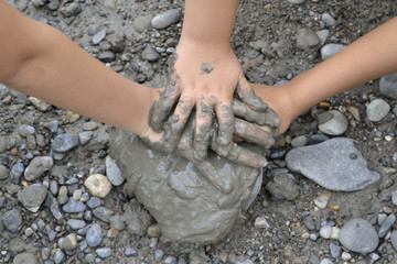 Manos de niño, una sobre otra, con barro, sobre una piedra.
