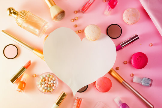 Make up products and macaroons flat lay layot with copy space on pink background, toned