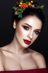 Beautiful woman portrait with red and yellow berries on head and with black hair and red lips.