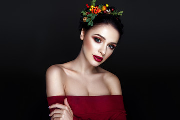 Beautiful woman portrait with red and yellow berries on head and with black hair and red lips.