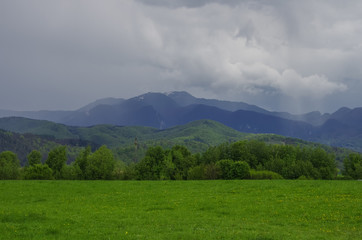 Green meadow with Fagaras mountains range at background, cloudy sky. Carpathians, Romania, Europe