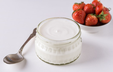 White yogurt in glass bowl with spoon and starwberries on rustic background.