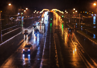 Evening traffic on the city avenue under a pouring rain. Beams of headlights, splashes, drops of a rain and fires in the distance in a defocusing.  