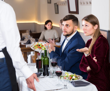 scowling guests conflicting with waiter in restaurant