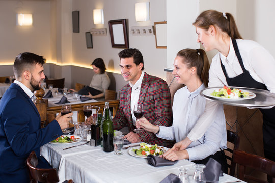 smiling waitress bringing delicious salads to smiling people at restaurant
