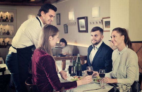  Positive waiter serving meals to friendly company guests