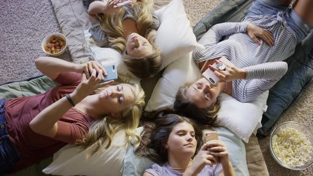 Medium high angle shot of girls laying on floor distracted by cell phones / Cedar Hills, Utah, United States