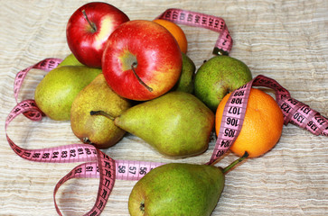 Healthy lifestyle. Fresh fruit and a centimeter tape: a diet for weight loss and harmony. Still life of apples, pears and tangerines closeup.