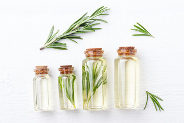Bottles with aromatic oil of rosemary on white wooden background. Top view.