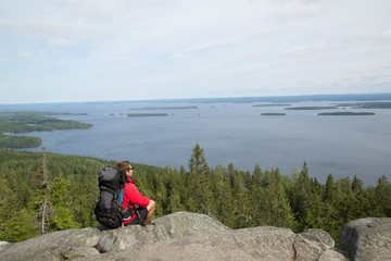 Hiker sits on the summit Ukko-Koli and enjoys the scenery of the Pielinen lake, summer 