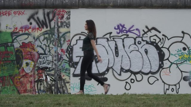 Wide slow motion shot of woman walking near wall with graffiti / Berlin, Germany