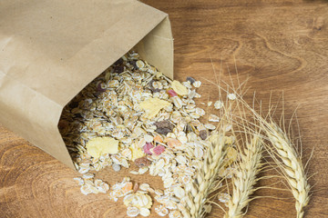 Muesli in a paper bag and ears on a wooden table. Granola in the package.