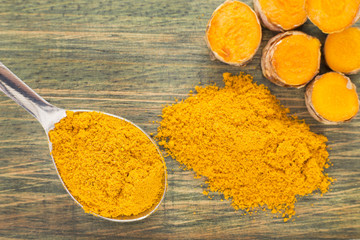 Turmeric powder and fresh turmeric on wooden background