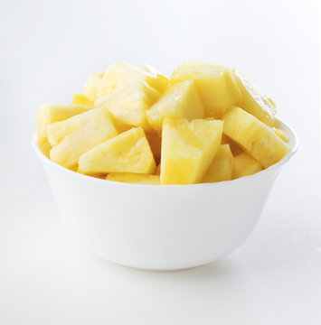 Pieces of pineapple in white bowl on white background