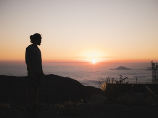 silhouette of man standing on the mountain above the clouds during sunset