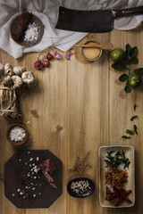 Thai food cooking ingredients with salt, garlic, dried chilli, pepper, lemon, sugar, knife, fabric and wooden chopping board on wooden board background. Top view with copy space in center