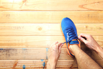 Young man tying laces of running shoes before training on wooden board