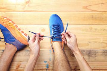 Young man tying laces of running shoes before training on wooden board