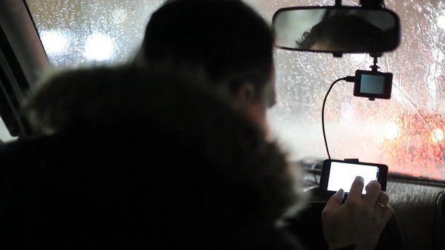A man gets into the car and turns on the navigator on the smartphone