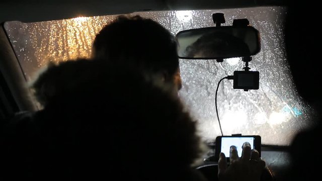A man gets into the car and turns on the navigator on the smartphone