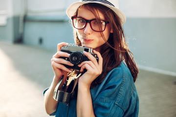 Summer closeup street portrait of young smiling beautiful and happy woman photographer posing with camera, wearing a hat