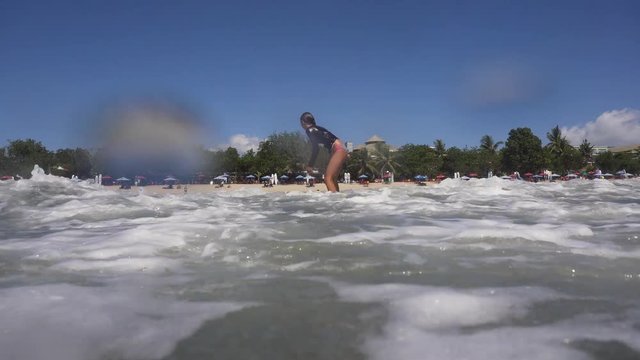 Young girl surfing in the ocean and having fun. Teenage girl in a surfing on the beah Kuta in Bali. Surfer with surf board. Lifestyle, people water sport adventure camp, beach extreme swim on summer