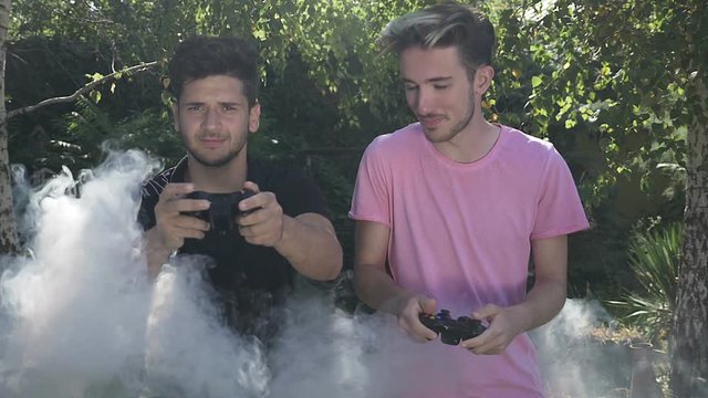 Slow motion of two friends in backyard intense playing video game using controllers smoke covering them concept of video games addiction in nature
