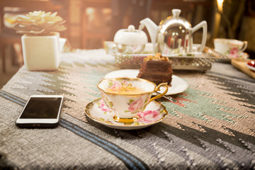 Cup of tea and slice of chocolate and tea pot with sunlight