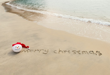 Obraz premium Merry Christmas written on tropical beach white sand with xmas snowman
