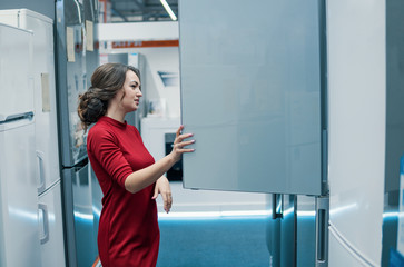 Smart modern female customer choosing large fridges in domestic appliances section. She looks happy