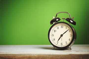 Retro alarm clock on wooden board with green background