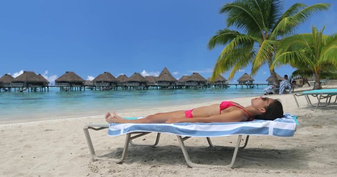 Vacation beach travel suntanning young woman on relaxing on beach in bikini. Sunbathing beautiful girl lying in sun lounger at luxury hotel resort with overwater bungalows. Paradise beach.