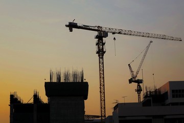 Construction cranes silhouetted against evening sky with clear orange sky. Industrial concept with copy space.