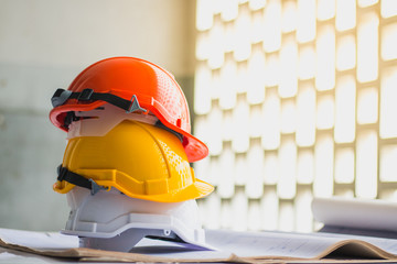 white, yellow and orange hard safety, helmet hat for safety project of workman or engineer on desk...
