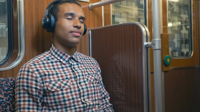 African man in a train car of the Berlin subway listening to music on headphones with pleasure