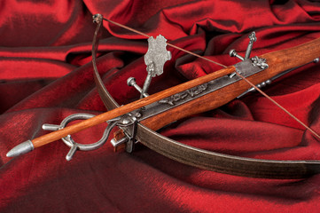 retro stylized wooden crossbow  close-up on crimson silk background
