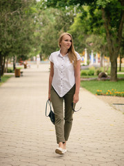 Beautiful woman with sunglasses in his left hand walks down the path in the Park.