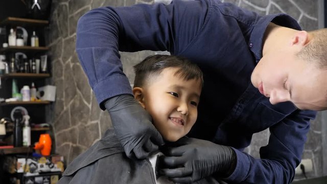 Barber covering the Asian kid with a cloak, the kid laughing 60 fps