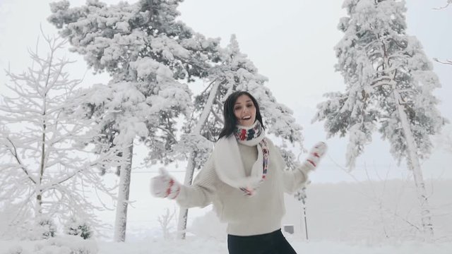 Young beautiful happy, smiling girl on the street catching snowflakes and joyfully jumping around and looking into the camera. Snowfall Christmas, New Year