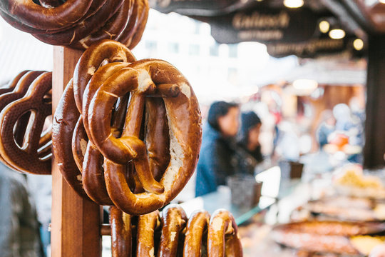 Traditional pretzels called Brezel hang on the stand against the background of a blurred street market and people on holiday.