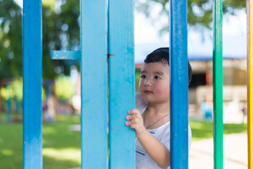 Obraz premium Smile Asian kid behind the colorful fence at playground in summer. shallow DOF.