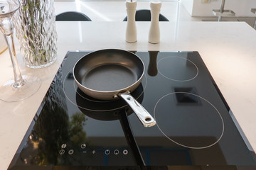 Frying pan on modern black induction stove, cooker, hob or built in cooktop with ceramic top in...